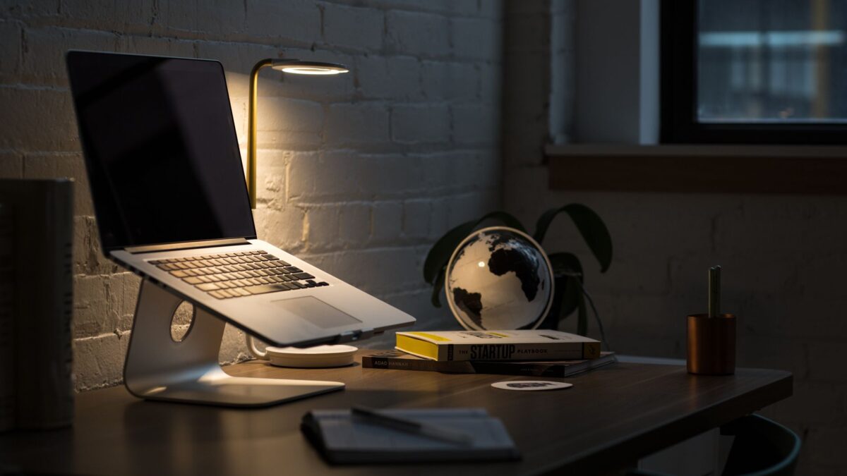 Laptop und Notizbuch auf dunklem Schreibtisch im warmen Lampenlicht