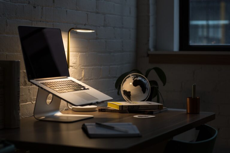 Laptop und Notizbuch auf dunklem Schreibtisch im warmen Lampenlicht